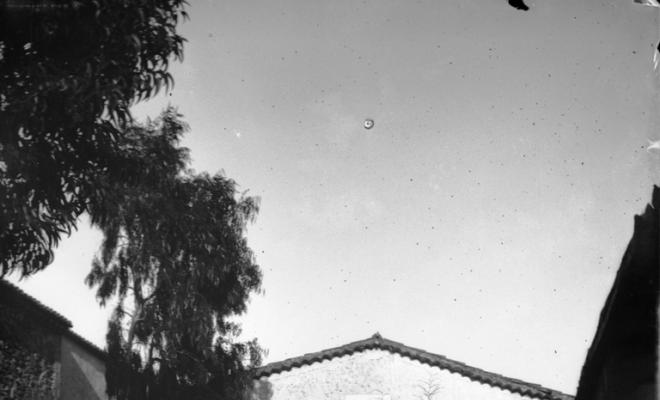 Caçadors davant una masia rodejats de gossos