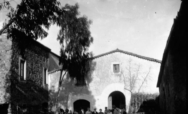 Caçadors davant una masia rodejats de gossos